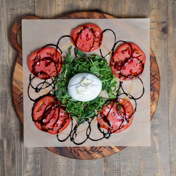 Fresh burrata, sliced tomatoes, arugula, and balsamic glaze on a rustic wooden board.