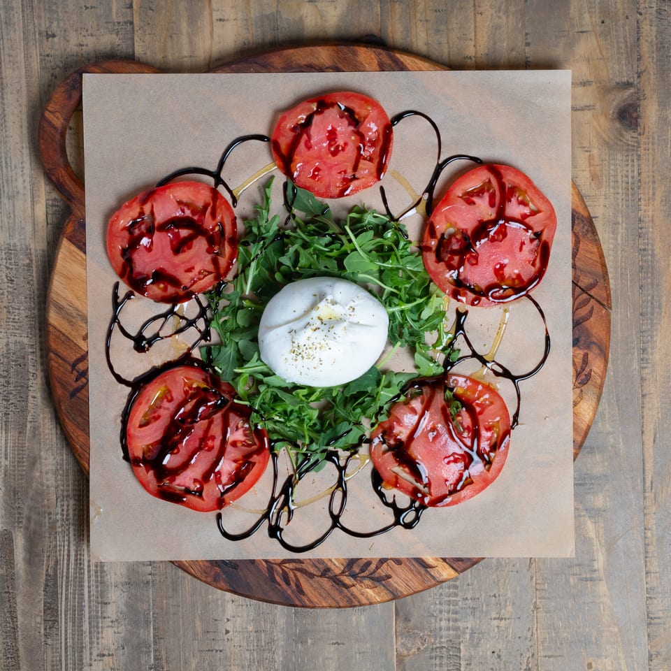 Fresh burrata, sliced tomatoes, arugula, and balsamic glaze on a rustic wooden board.