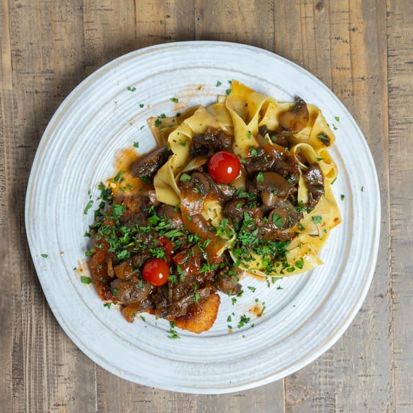 Plate of pappardelle pasta with mushroom ragu, breaded cutlet, cherry tomatoes, and fresh parsley.