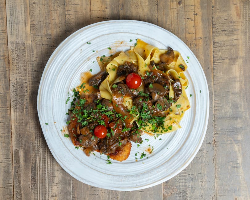Plate of pappardelle pasta with mushroom ragu, breaded cutlet, cherry tomatoes, and fresh parsley.