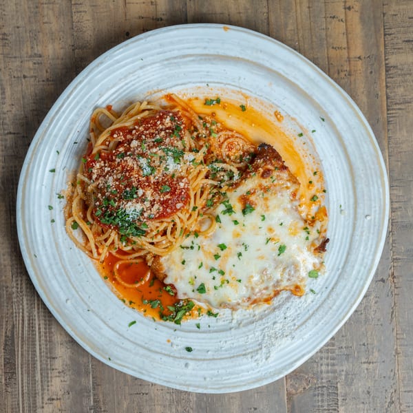 Spaghetti with marinara sauce and chicken parmesan, garnished with cheese and parsley on a white plate.