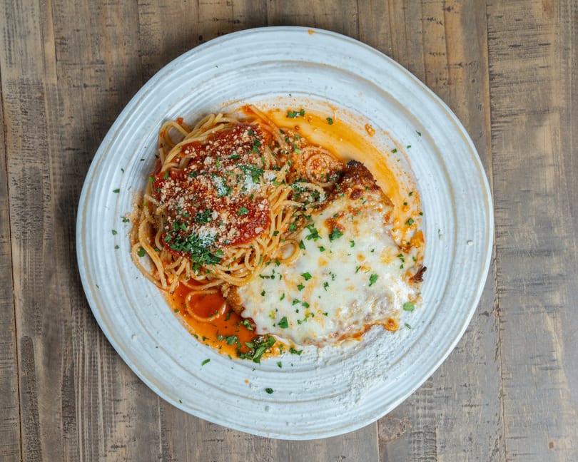 Spaghetti with marinara sauce and chicken parmesan, garnished with cheese and parsley on a white plate.