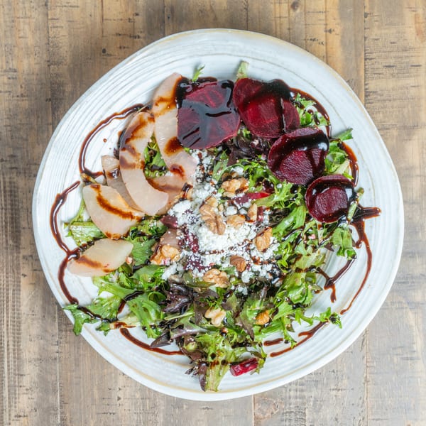 Fresh salad with mixed greens, sliced pears, beets, crumbled cheese, walnuts, and balsamic glaze.