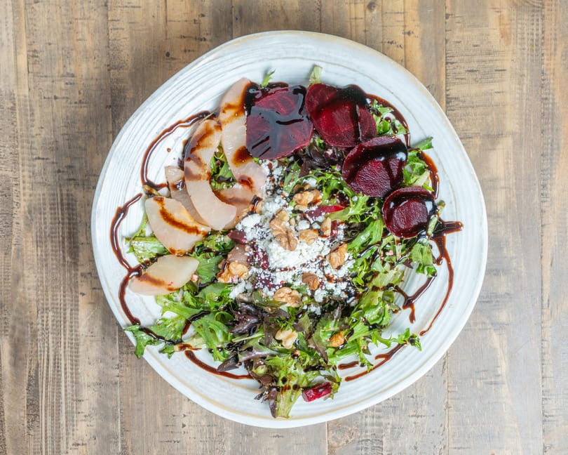 Fresh salad with mixed greens, sliced pears, beets, crumbled cheese, walnuts, and balsamic glaze.