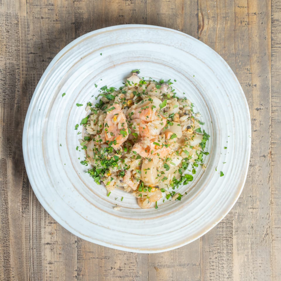 Creamy seafood rice dish with shrimp, scallops, and fresh parsley on a rustic wooden table.