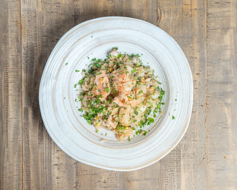 Creamy seafood rice dish with shrimp, scallops, and fresh parsley on a rustic wooden table.