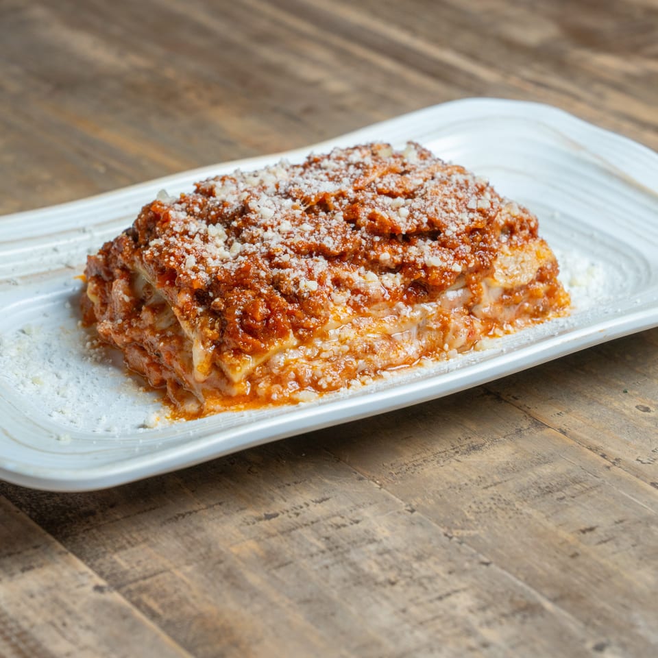 Generous serving of cheesy lasagna with rich red sauce and grated Parmesan on a white plate.