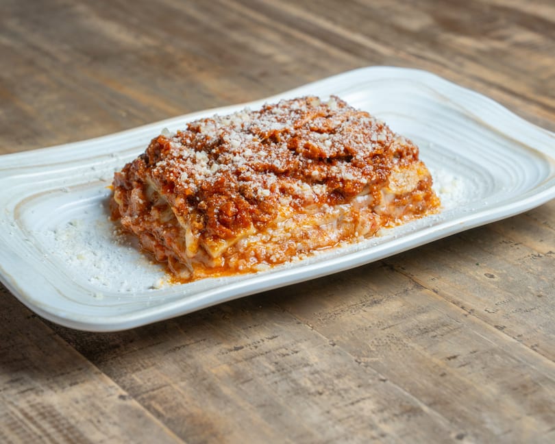 Generous serving of cheesy lasagna with rich red sauce and grated Parmesan on a white plate.