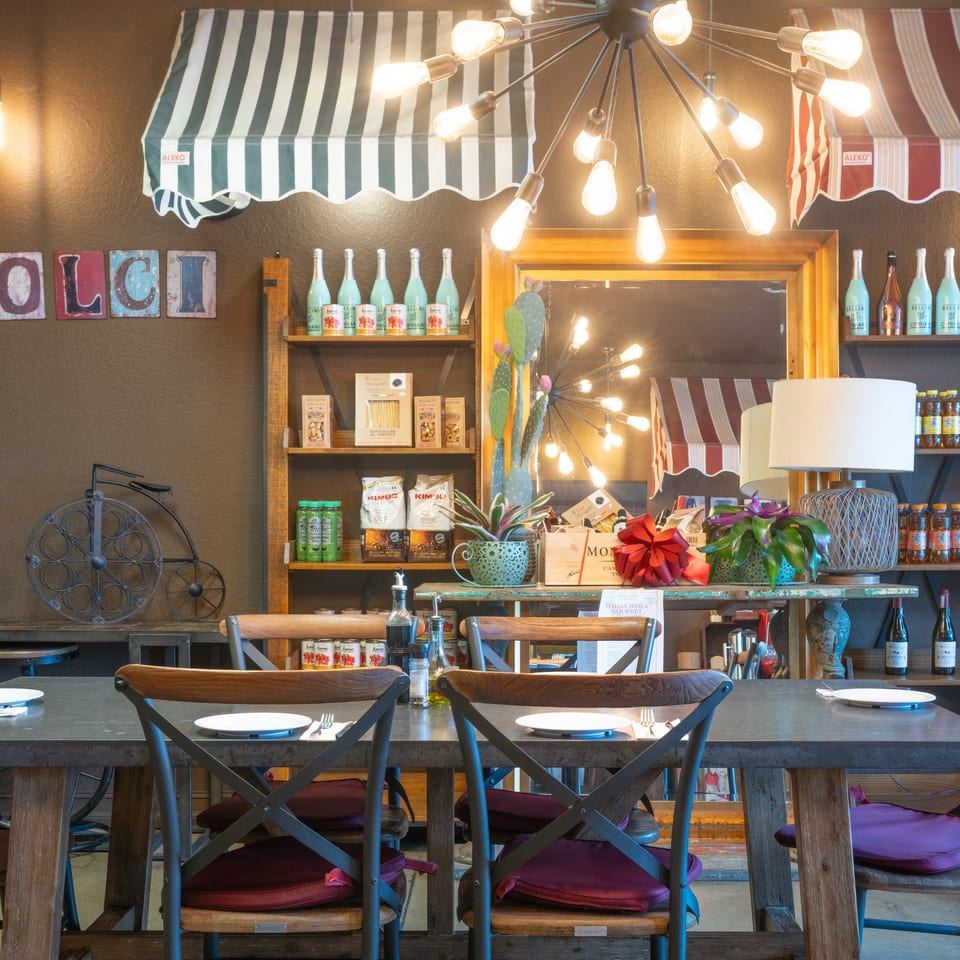 Warm Italian restaurant interior with dining tables, shelves of gourmet products, and striped awnings.