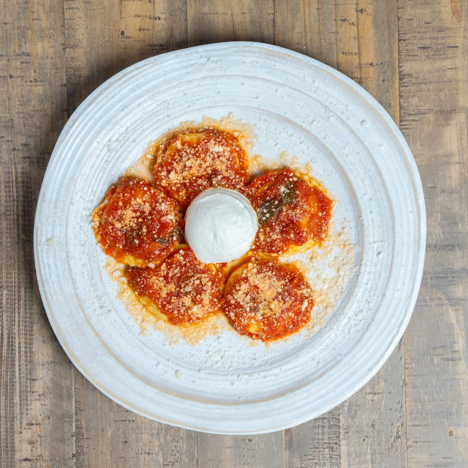 Five ravioli with red sauce and parmesan cheese, with a dollop of burrata in the center.