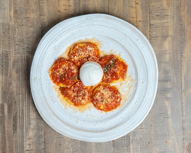 Five ravioli with red sauce and parmesan cheese, with a dollop of burrata in the center.