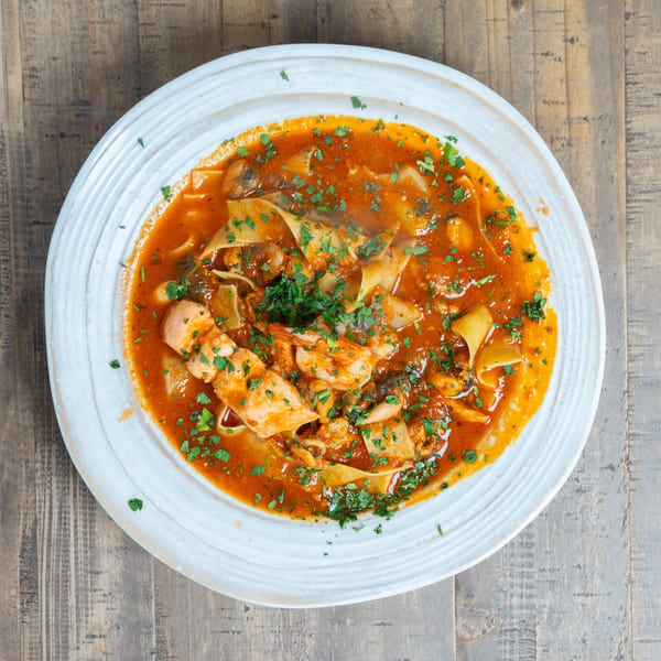 Seafood pasta with wide noodles, shrimp, mussels, and fish in a red sauce, garnished with parsley.