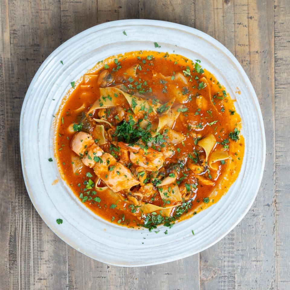 Seafood pasta with wide noodles, shrimp, mussels, and fish in a red sauce, garnished with parsley.