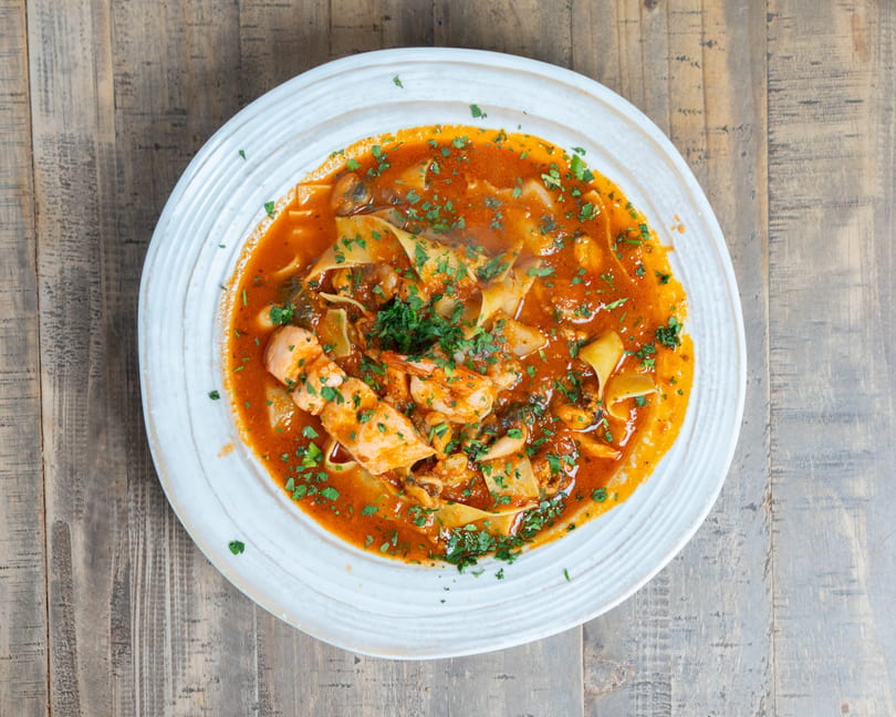Seafood pasta with wide noodles, shrimp, mussels, and fish in a red sauce, garnished with parsley.